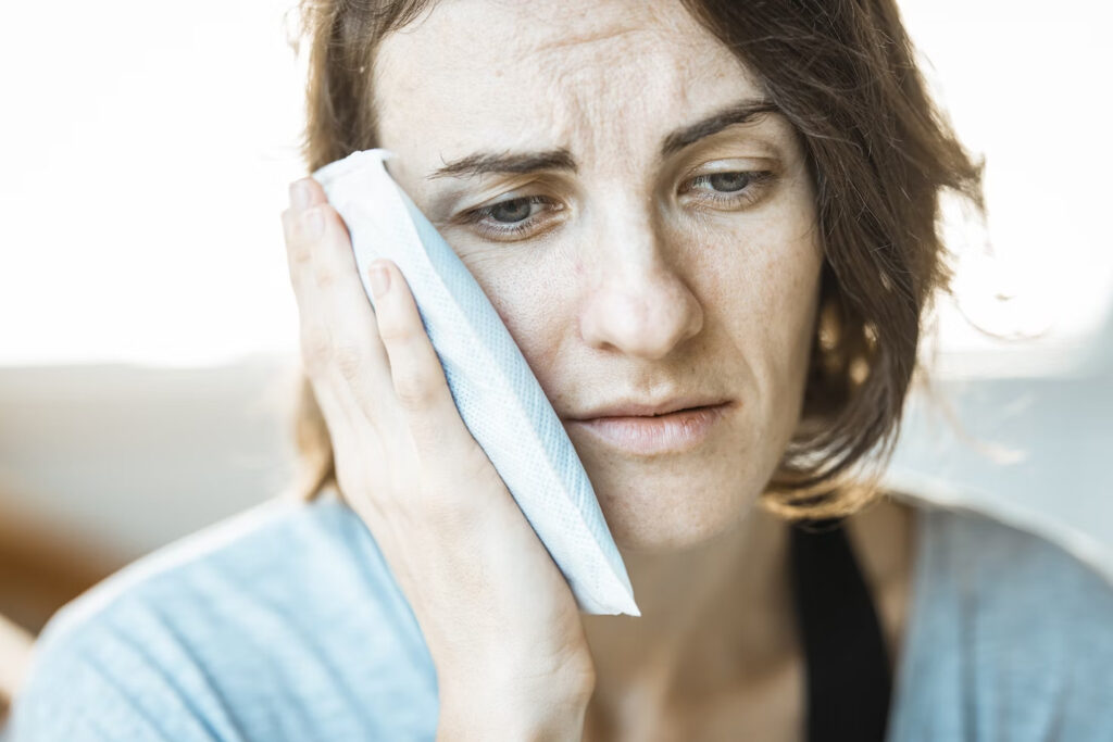 a woman frowning in pain while holding a cold compress to her jaw and cheeks