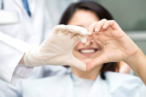 smiling patient and dentist forming heart hands together